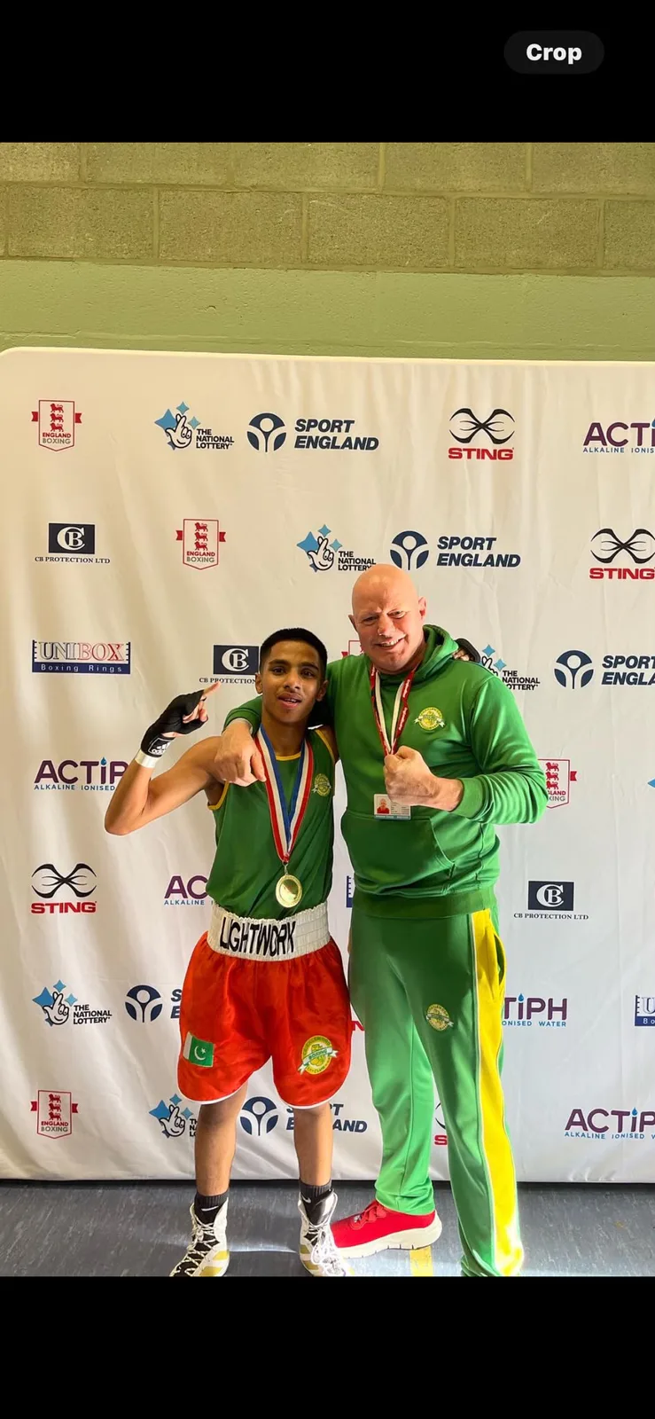 A Cricklewood boxer wearing a gold medal with his coach